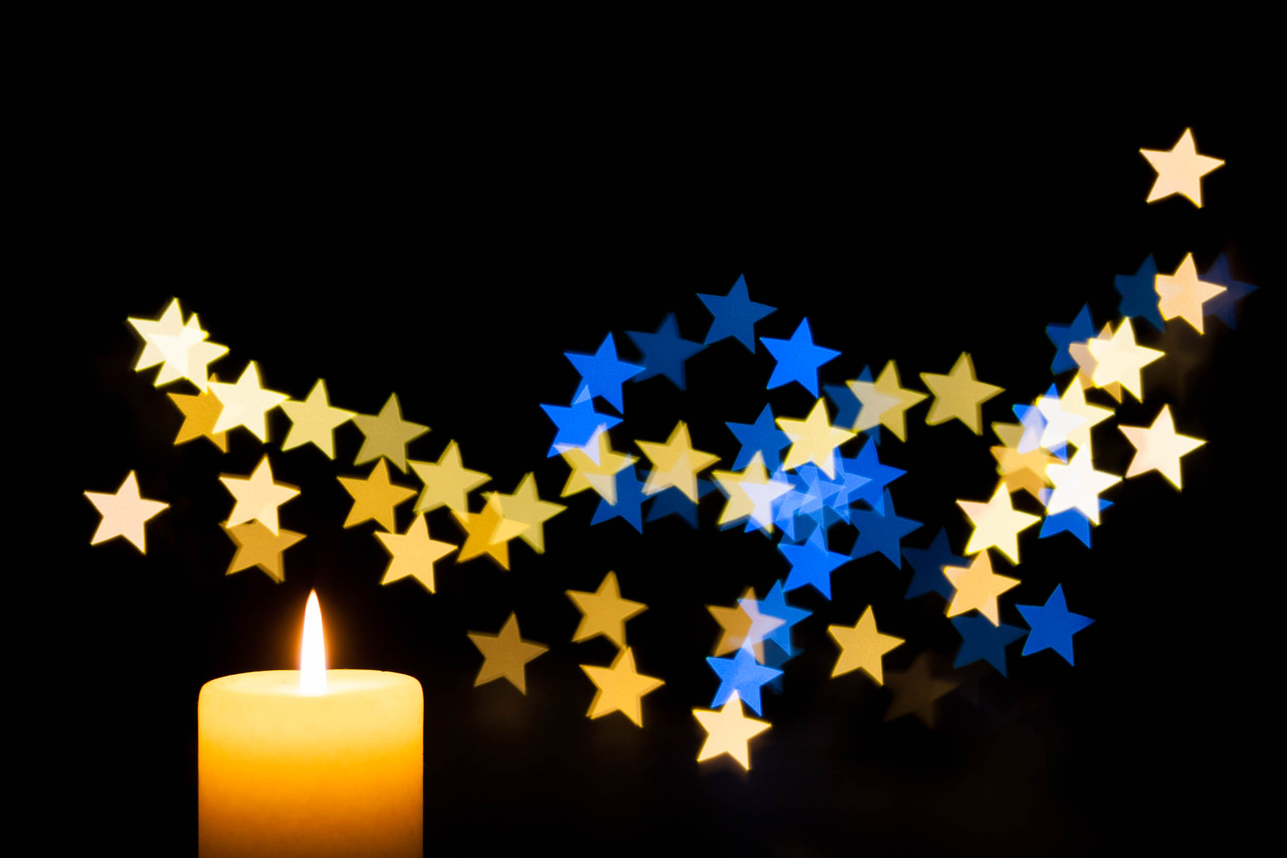Brennende Kerze mit goldenen und blauen Sternen vor schwarzem Hintergrund